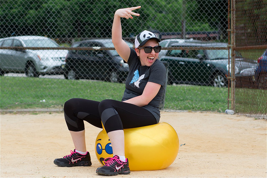 Woman sitting on a yellow bouncy ball making a peace sign with her hand.